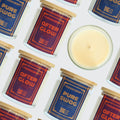 A styled flat-lay of Moodcraft 'After Glow' scented candles, showing several glass jars with blue and red labels and a single open candle displaying its pale yellow wax on a white background.