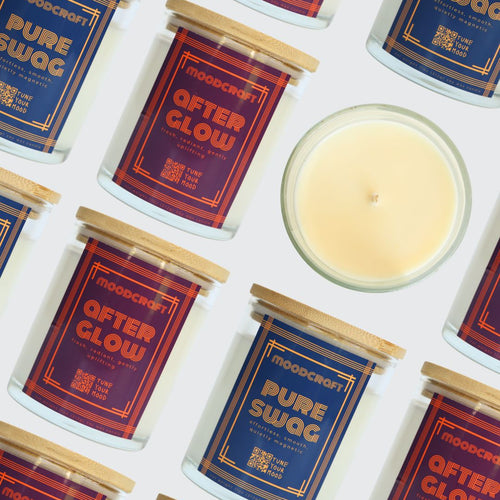 A styled flat-lay of Moodcraft 'After Glow' scented candles, showing several glass jars with blue and red labels and a single open candle displaying its pale yellow wax on a white background.