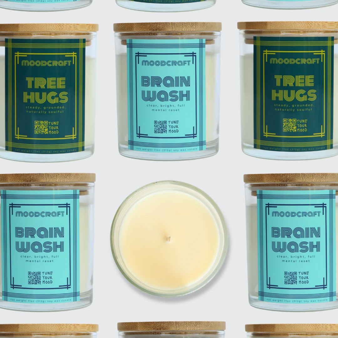 A grid-style product collage showing multiple Moodcraft candles on a white background, with two jars labeled Tree Hugs and two jars labeled Brain Wash, plus one open candle centered below showing pale cream wax.