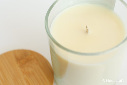 Candle in a glass jar with a wooden coaster on a white background