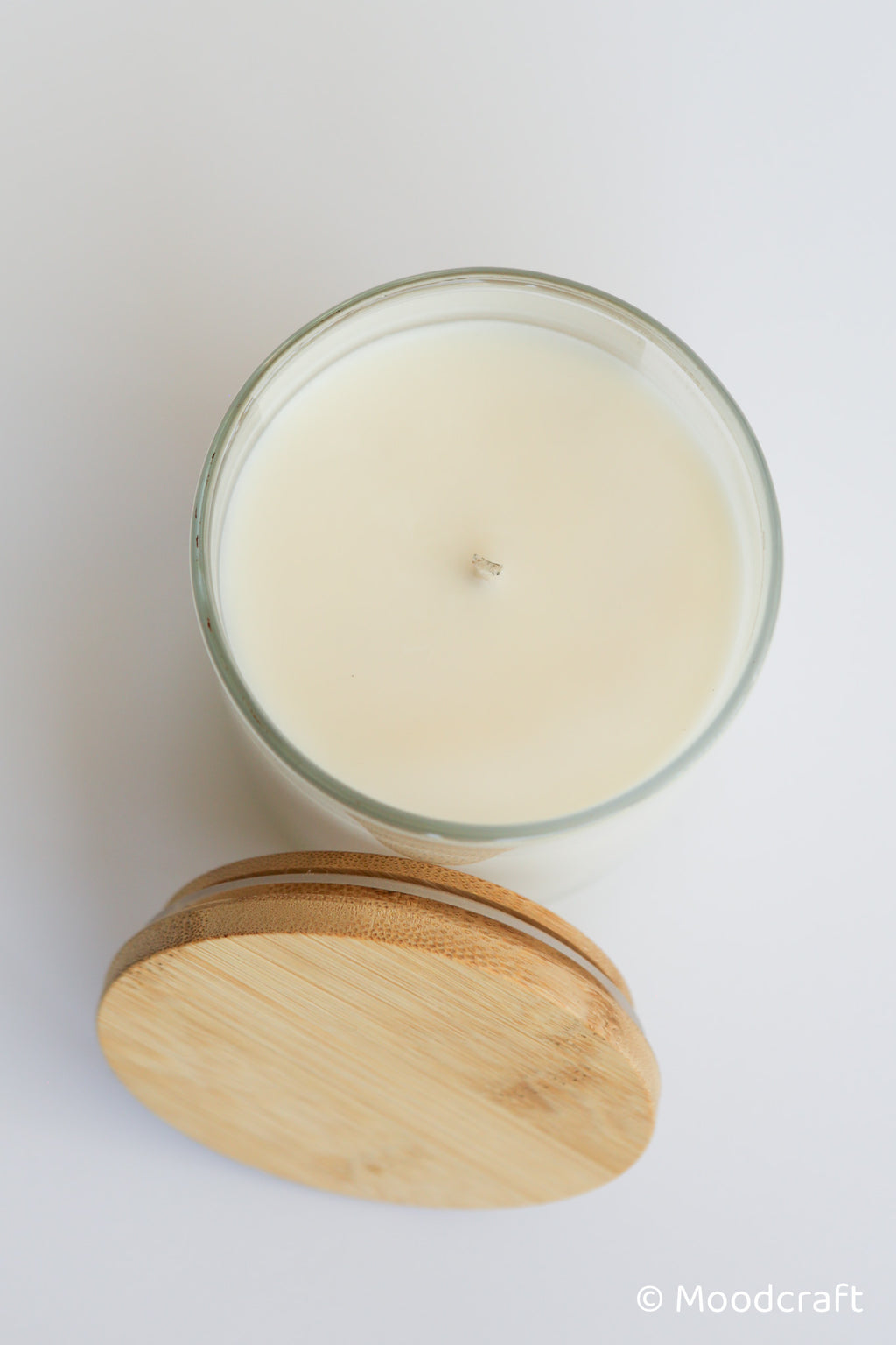Glass candle with wooden lid on a white background, branded 'Moodcraft'.
