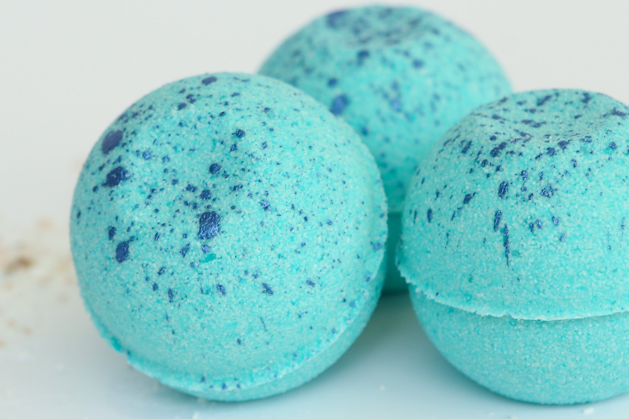 Three blue speckled bath bombs on a light background