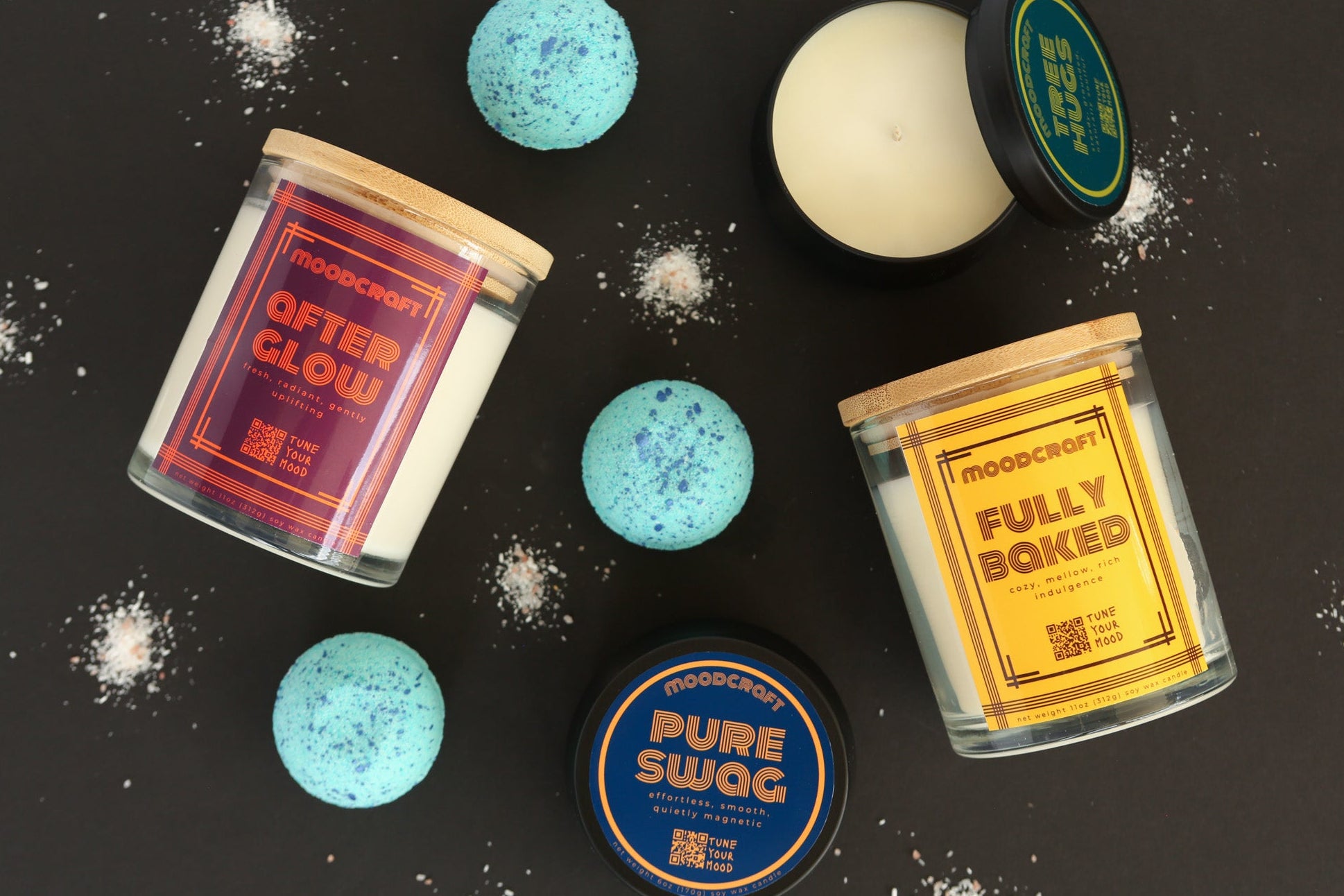 Collection of bath bombs and candles with visible branding on a dark surface.