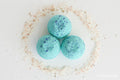 Three blue bath bombs with speckles on a bed of sand-like material.